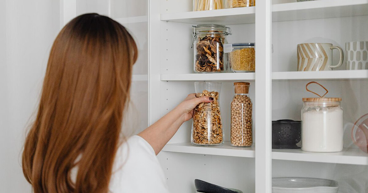 Woman reaches in to open kitchen cabinet grabbing bottle of nuts
