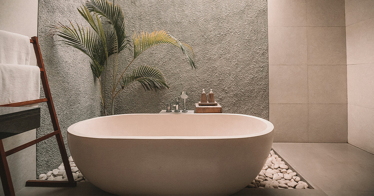 Freestanding bath on tiles with pebbles for flooring behind bath