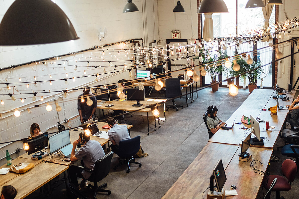 Open coworking space with shared furniture and festoon lighting hanging above workers