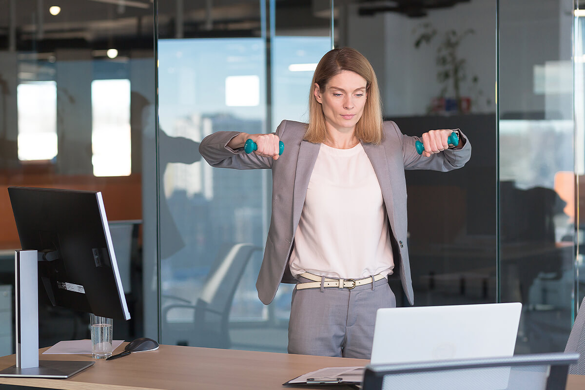 Business woman lifting small weights at office desk to get some movement while reading document