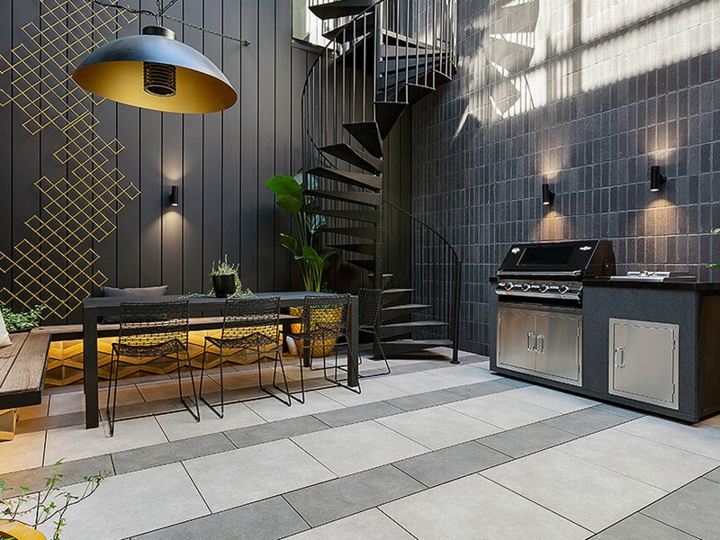 Designer courtyard in modern home with dark tiles, gold accents and green plants throughout with circular feature stairs in back corner