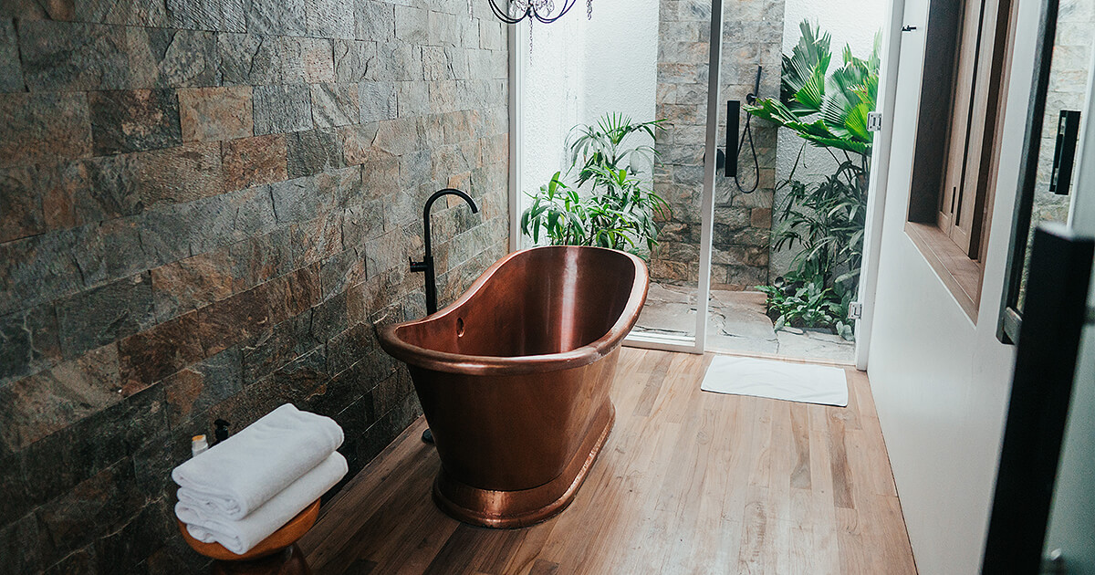 Stone tines in bathroom with copper look bath and timber flooring in natural light